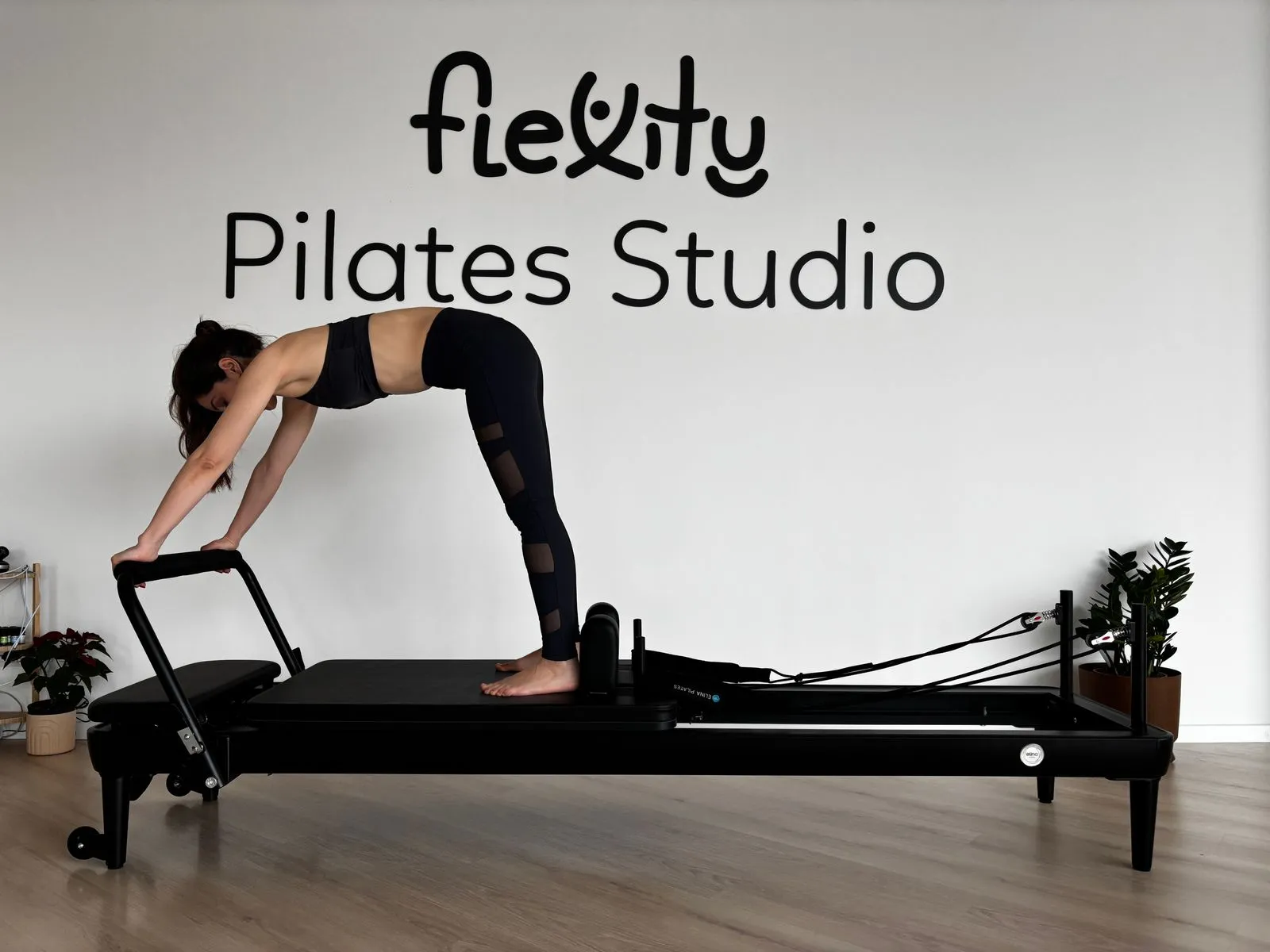 Woman performing Pilates on reformer machine in minimalist studio.